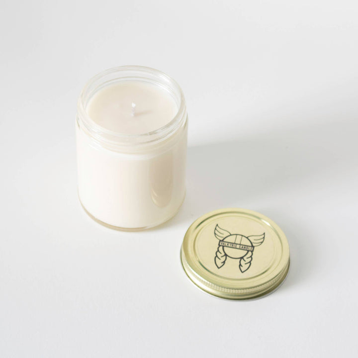 White candle in a glass jar with a decorative lid on a white background
