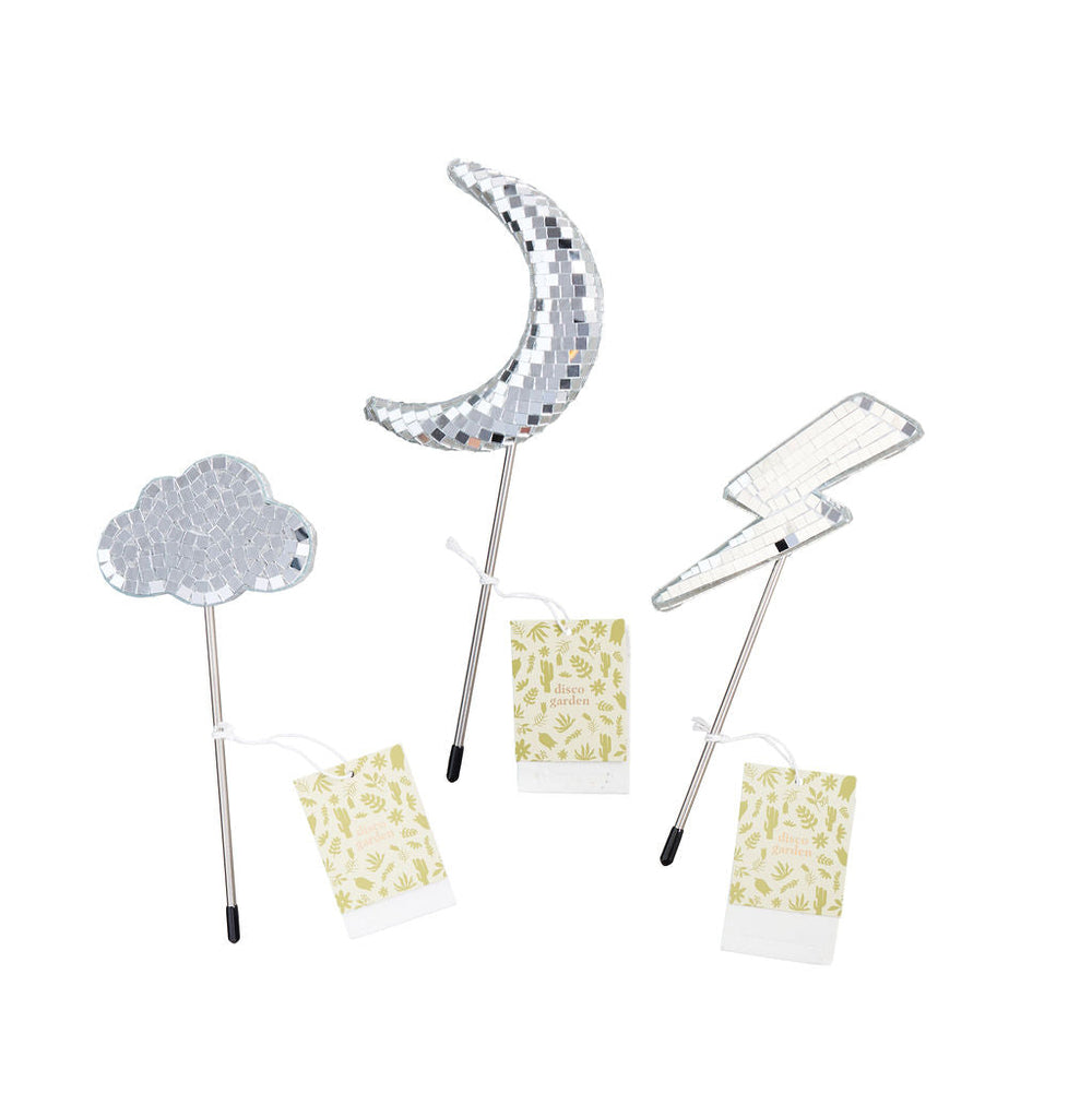 Decorative disco ball plant stakes shaped like a cloud, moon and lightning bolt each with a branded plantable botanical hangtag laid out over a plain white background.
