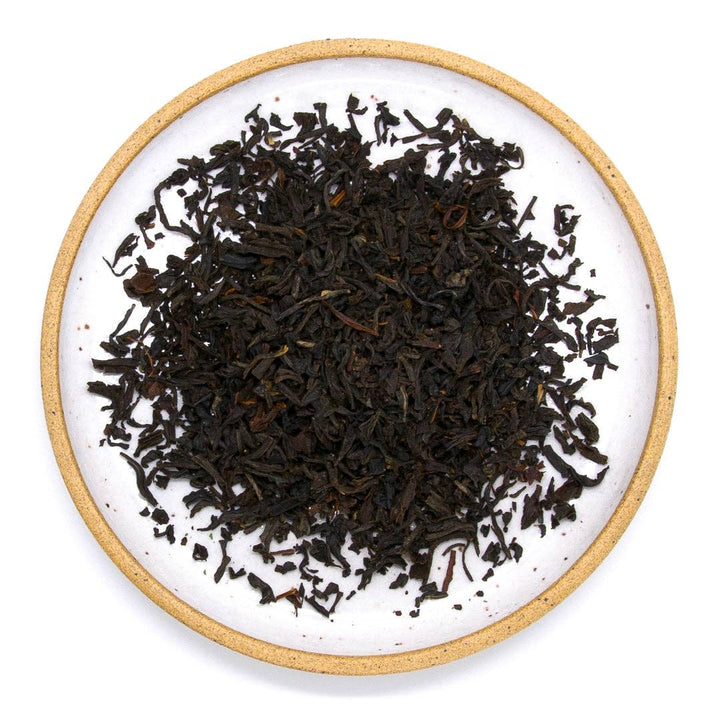 Dry black tea leaves on a white plate with a gold rim