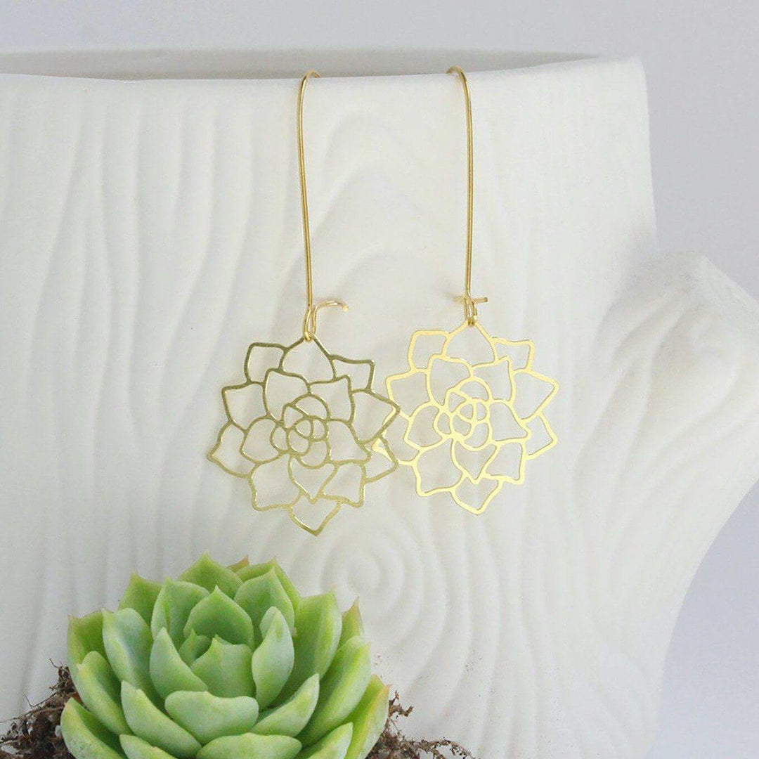 Elegant gold succulent rosette earrings hang in front of a white background and live succulent plant